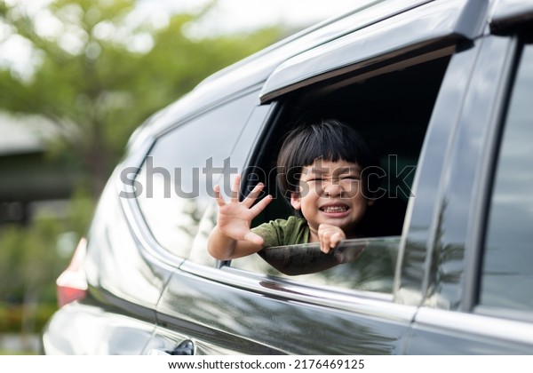 Happy\
asian boy waving hands gesturing hello out of the car window during\
a trip with his family. Little child sticking head outta the\
windshield traveling in a car on a summer\
vacation.