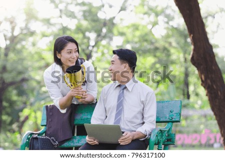 Happy asian business couple associates after receiving awards from work in the park.