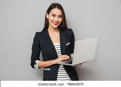 Happy Asian Business Woman Holding Laptop Computer And Looking At The Camera Over Gray Background