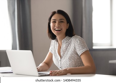 Happy Asian Business Woman Laughing Sitting At Work Desk With Laptop, Cheerful Smiling Female Chinese Employee Having Fun Feeling Joy And Positive Emotion Express Sincere Laughter At Office Workplace