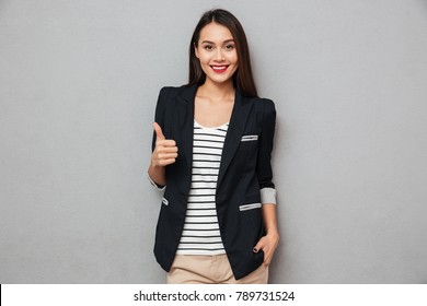 Happy asian business woman showing thumb up and looking at the camera over gray background - Powered by Shutterstock