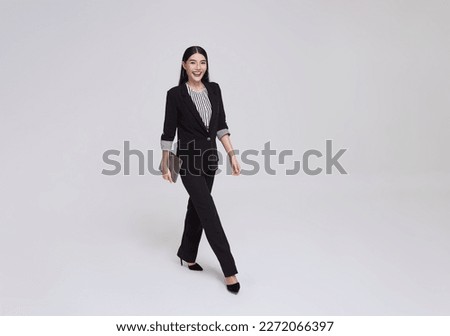 Happy Asian business woman smile in formal suit holding tablet and walking over gray background. Stock photo © 