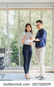 Happy Asian Businessman And Woman Discussing New Business Project In Tablet In Modern Meeting Room.