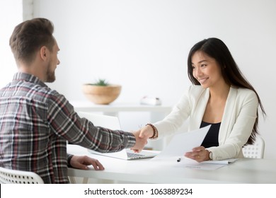 Happy Asian Businesswoman Handshaking Successful Caucasian Candidate Holding Employment Agreement Offering Job Contract, Smiling Friendly Employer Shaking New Hire Hand, Diverse Partners Making Deal