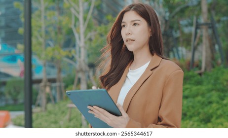 Happy Asian Businesswoman Planning in an Outdoor Workspace. Hybrid Work in Urban Greenery, Smiling Business woman Using Tablet. Joyful Manager Writing Emails in a Park., Remote Work Lifestyle - Powered by Shutterstock