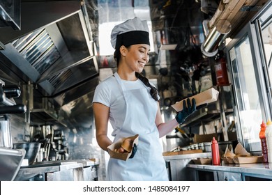 happy asian chef in hat holding carton plates in food truck 