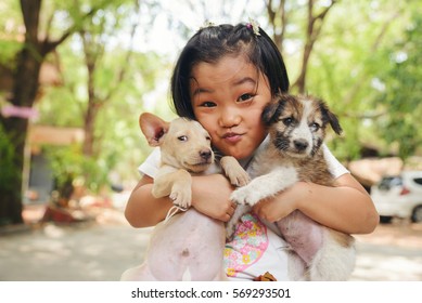 Happy Asian Child Playing With Thai Dog. Homeless Poor Kid Holding Cute Pet In The Park