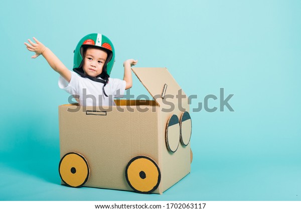 Happy Asian children boy with Helmet smile in\
driving play car creative by a cardboard box imagination, summer\
holiday travel concept, studio shot on blue background with copy\
space for text