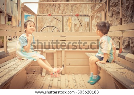 Happy Asian children are riding on a truck. Smiling Asian siblings sitting on different side on a military truck with copy space in the middle.