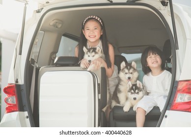 Happy asian children and siberian husky puppies sitting in the car