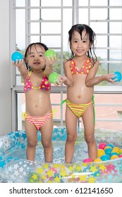 Happy Asian Chinese Little Sisters Playing In The Inflatable Pool Inside The House.