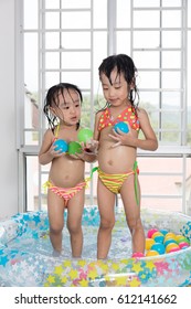 Happy Asian Chinese Little Sisters Playing In The Inflatable Pool Inside The House.