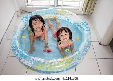 Happy Asian Chinese Little Sisters Playing In The Inflatable Pool Inside The House.