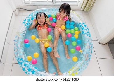 Happy Asian Chinese Little Sisters Playing In The Inflatable Pool Inside The House.