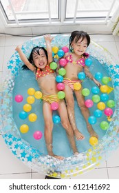 Happy Asian Chinese Little Sisters Playing In The Inflatable Pool Inside The House.