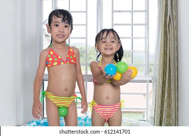 Happy Asian Chinese Little Sisters Playing In The Inflatable Pool Inside The House.