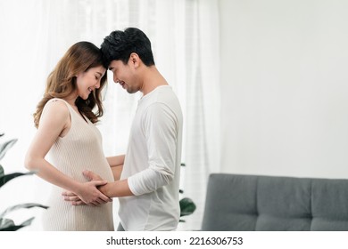 A happy asian couple. A beautiful pregnant wife and her  handsome husband are smiling happily with their heads touched and their hands grabbing the wife's tummy to feel their baby. - Powered by Shutterstock