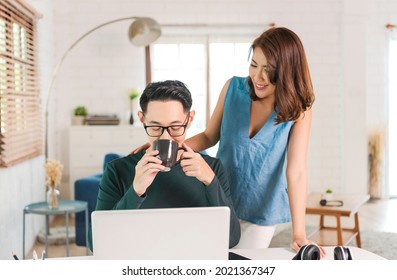 Happy Asian Couple Drinking Coffee On Desktop Computer At Home Office. 
