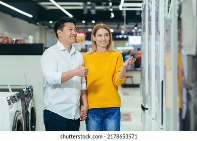 Happy Asian Couple Family Man And Woman Make A Choice Choose Of New Household Home Appliances In Supermarket Survey Refrigerator Fridge Cooler, Freezer, Cold Store Purchase And Shopping