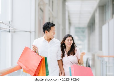 Happy Asian Couple Holding Colorful Shopping Bags And Enjoying Shopping, Having Fun Together In Mall. Consumerism, Love, Dating, Lifestyle Concept