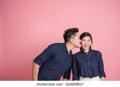 Happy Asian couple kissing on pink bacground. Man is kissing his girlfriend in cheek