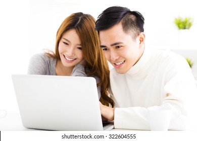 Happy Asian Couple Looking At Laptop In Living Room