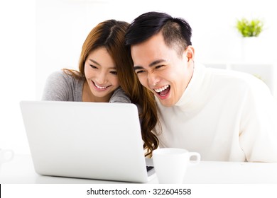 Happy Asian Couple Looking At Laptop In Living Room