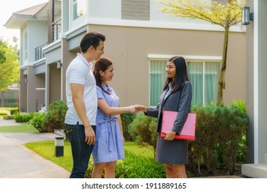 Happy Asian Couple Looking For Their New House And Shake Hands With Real Estate Broker After A Deal. Young Couple Handshaking Real Estate Agent After Signing Contract For Buy House.
