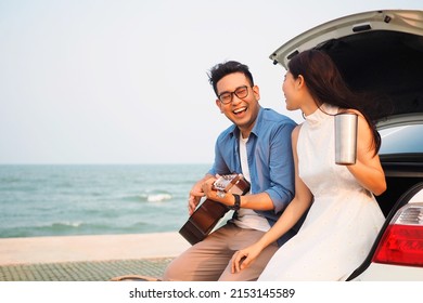 Happy Asian couple lover having stop off by the sea and sitting in hatchback  ,they are  drinking coffee playing guitar together. - Powered by Shutterstock