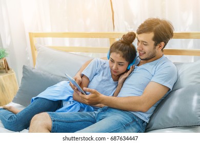 Happy Asian Couple Lying On The Bed. Lover Using Smart Tablet Listen Music And Shopping Online Together In Bedroom. Concept Of Family Relax In Living Room.