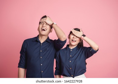 Happy Asian Couple Make Funny Facepalm Gesture With Eye Close Over Pink Background 