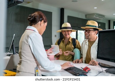 Happy Asian couple man and woman walking to airline ground staff at check in counter and get boarding pass ticket in airport terminal. Airline service business and airplane transportation concept