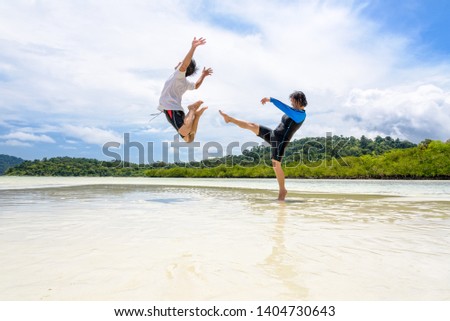 Happy asian couple play fun activity together woman show the teasing position, kicking a man to bounce far away on the beach of Ko Ra Wi near Ko Lipe island, Tarutao National Park, Satun, Thailand