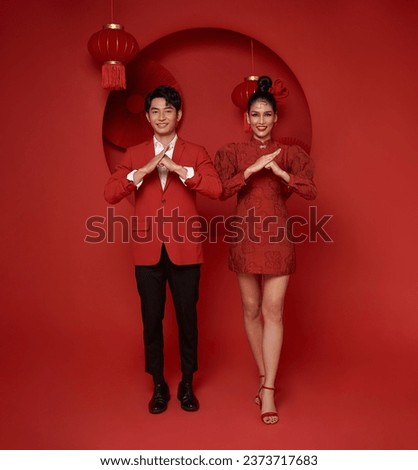 Happy asian couple in red casual attire with gesture of congratulation greeting happy new year 2024 on Decoration traditional red background.