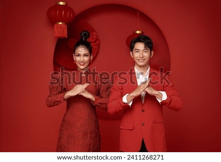 Happy asian couple in red casual attire with gesture of congratulation greeting happy chinese new year 2024 on Decoration traditional red background.
