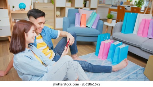 Happy Asian Couple Shopping Online By Smartphone With Many Bags At New Home