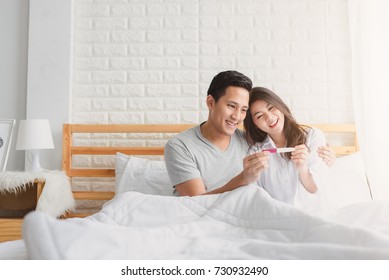 Happy Asian Couple Smiling After Find Out Positive Pregnancy Test In Bedroom At Home