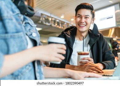 Happy Asian Couple Take Off Face Mask In A Coffee Shop Surfing Internet On Laptop. Young Man And Woman In A Restaurant Looking At Touch Screen Computer Laugh Smile Together