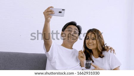 Happy asian couple taking photos together in living room.