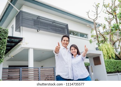 Happy Asian Couple With Thumb Up Standing Together In Front Of Thier House