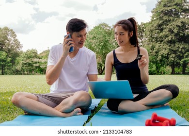 Happy Asian Couple Using Laptop Shopping To Order Fitness Equipment Online From Credit Card After Doing Gym Activity In Young Woman Using Smartphone Hotspot Connected Online For Convenience.