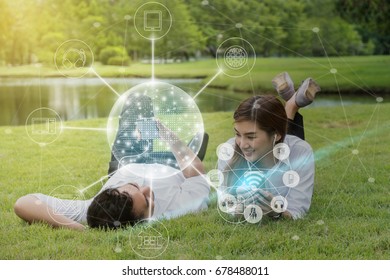 Happy Asian Couple Using And Listening The Song And Using The Social Network Via Smart Mobile Phone For Online Shopping With Omni Channel In The Park, Lifestyle And Technology Concept