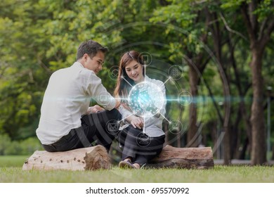 Happy Asian Couple Using And Listening The Song And Using The Social Network Via Smart Mobile Phone For Online Shopping With Omni Channel In The Park, Lifestyle And Technology Concept