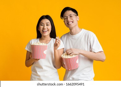 Happy Asian Couple Watching Funny Movie, Eating Popcorn, Yellow Background