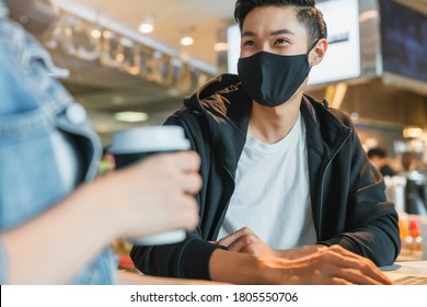 Happy asian couple wear face mask virus protection in a coffee shop enjoy good conversation. Young man and woman in a restaurant looking at touch screen computer laugh smile together - Powered by Shutterstock