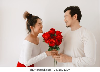 Happy Asian couples holding and giving red roses, both woman and man smiling looking to each other, enjoy good time on Valentines, isolated over white wall, proposal engage woman, begging love. - Powered by Shutterstock