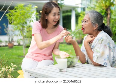 Happy Asian Daughter Have Lunch Whit Her Family And Feeding Salad To Mother In Backyard.