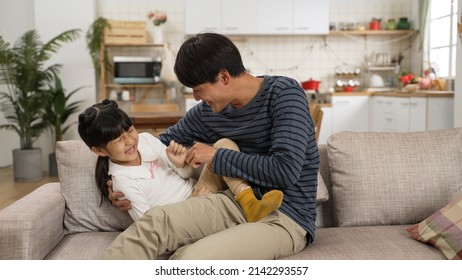 Happy Asian Daughter Having Fun Massaging Her Father’s Back At Home. The Man Getting Up From Sofa And Tickling The Giggling Girl As She Is Hitting Hard On His Body