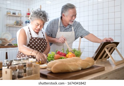 Happy Asian Elder Senior Couple Cooking Fresh Meal In Kitchen At Home.