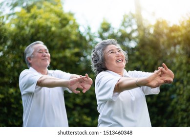 Happy Asian Elderly Couple Stretching Hands Before Exercise Over Green Nature At Park Outdoor. Happy Smiling Old People In White Shirts Workout. Health Care